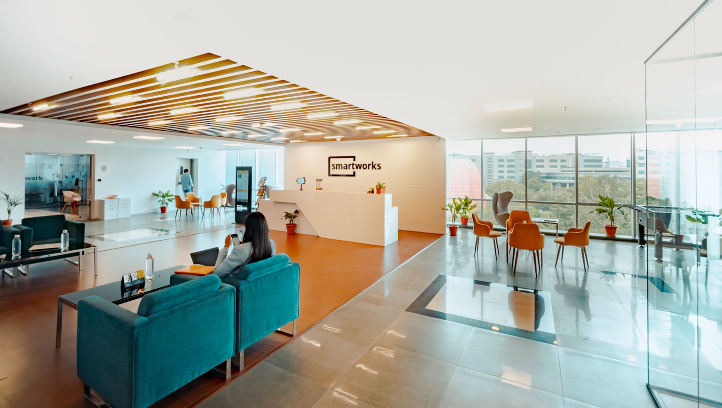 Nő telefonozik egy modern irodai recepció teal színű kanapéján.