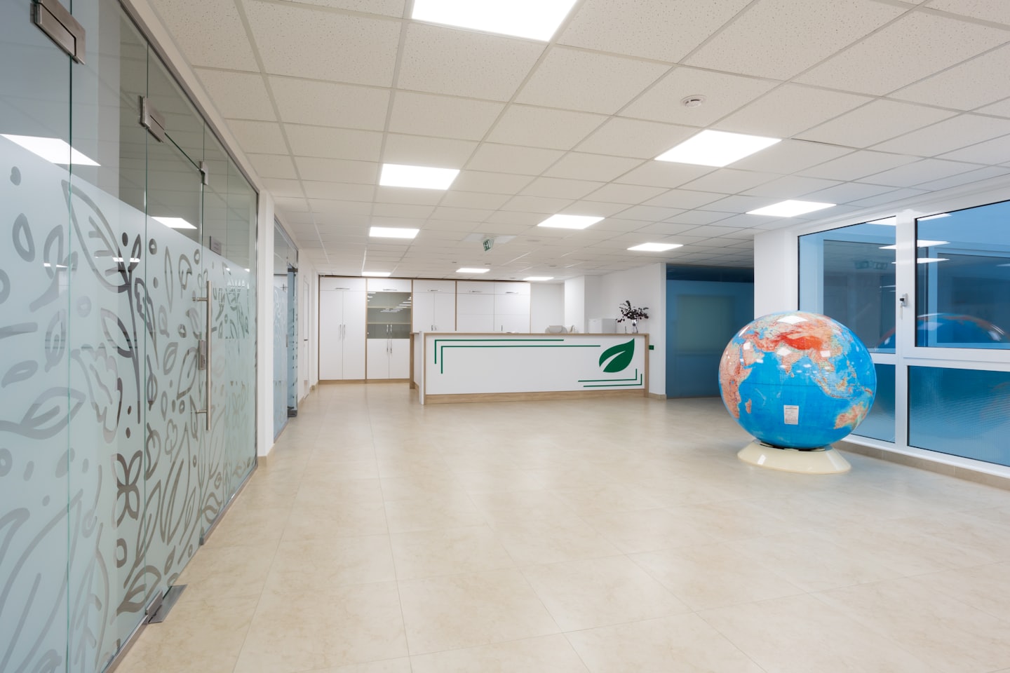 Modern irodai recepciós pult földgömbbel és matt üveg válaszfalakkal.
